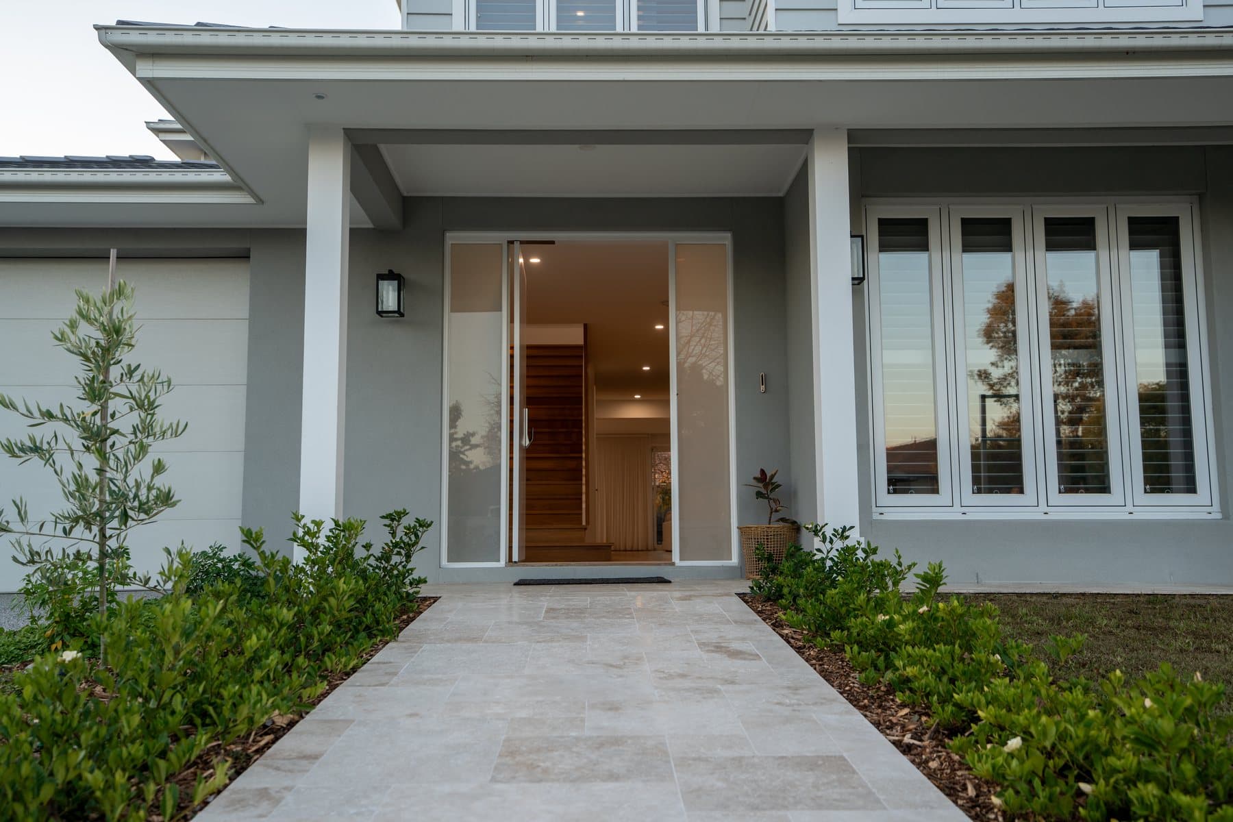 Covered portico with white columns, a travertine path and a glass pivot door at The Willow, Rowville