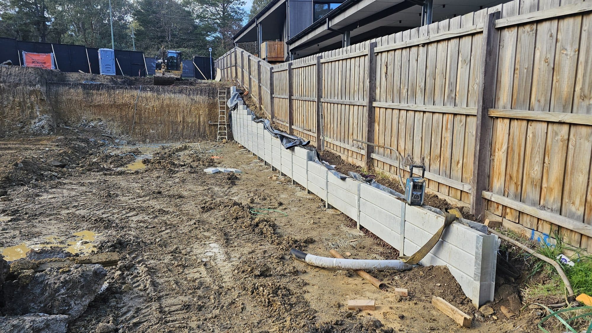Concrete sleeper retaining wall being built along a side boundary fence on an excavated sloping block