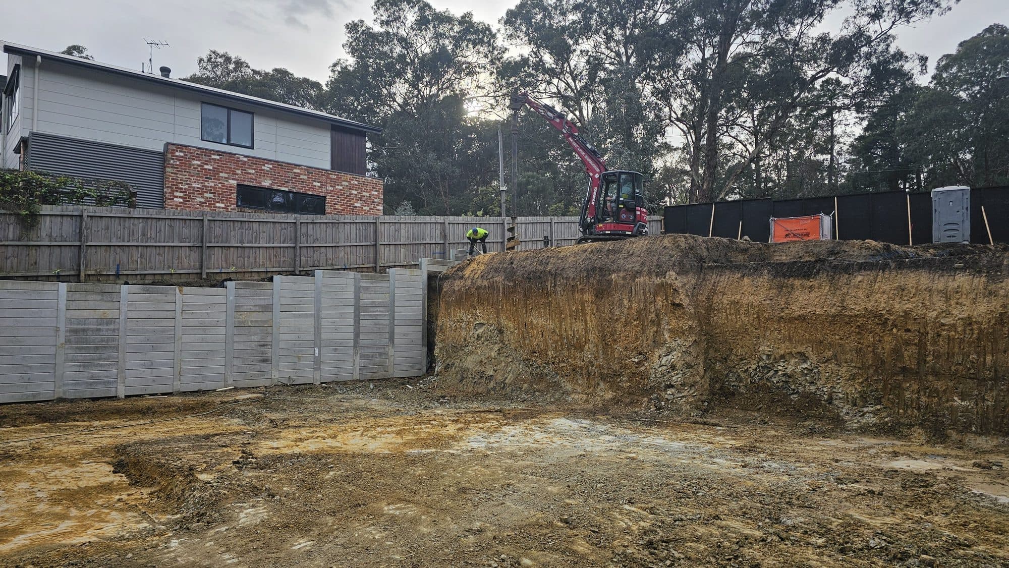 Concrete sleeper retaining wall beside an open excavation cut face on a sloping Warrandyte block
