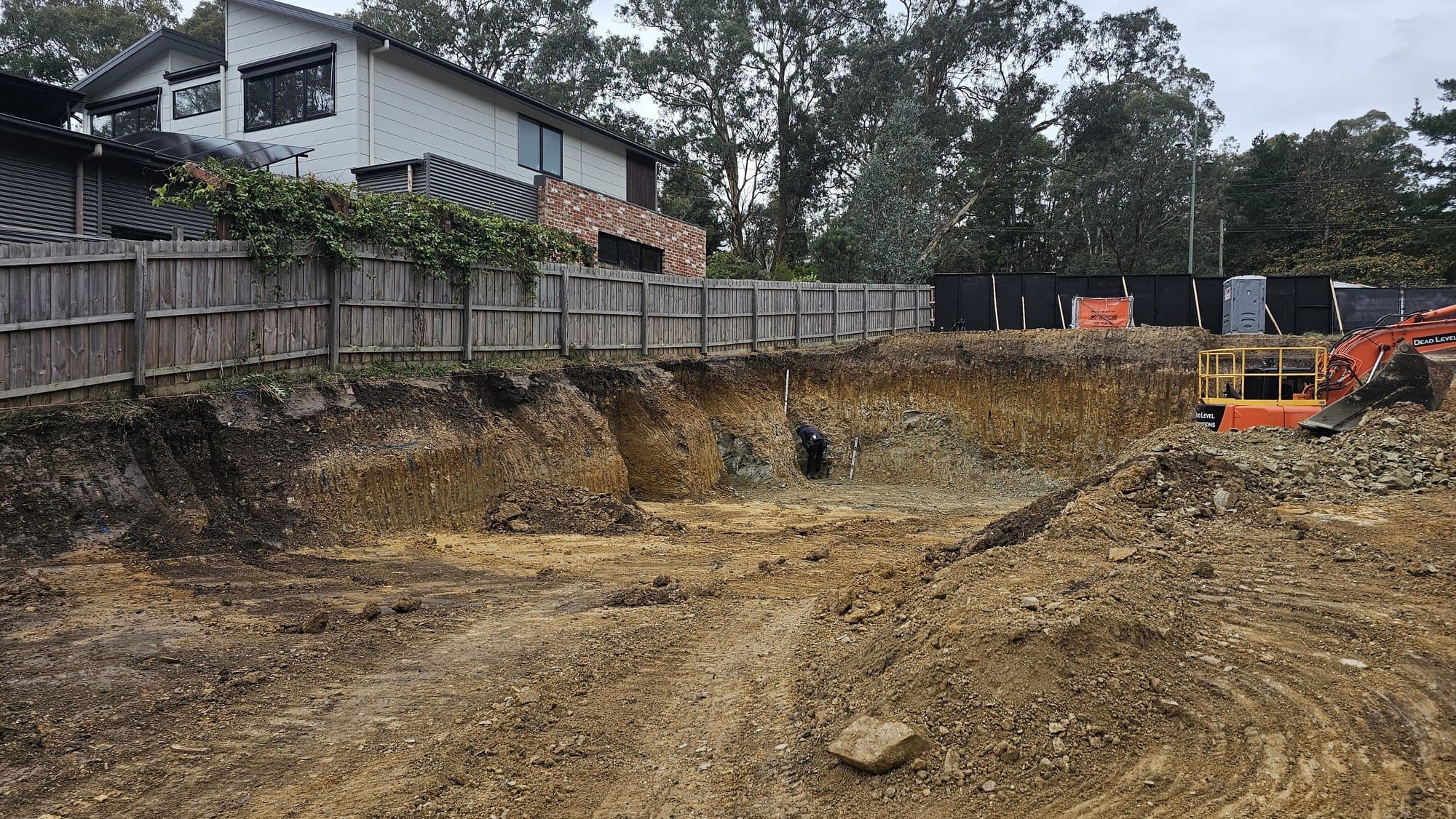 Bulk excavation into a steep sloping block in Warrandyte, with an excavator and exposed cut face