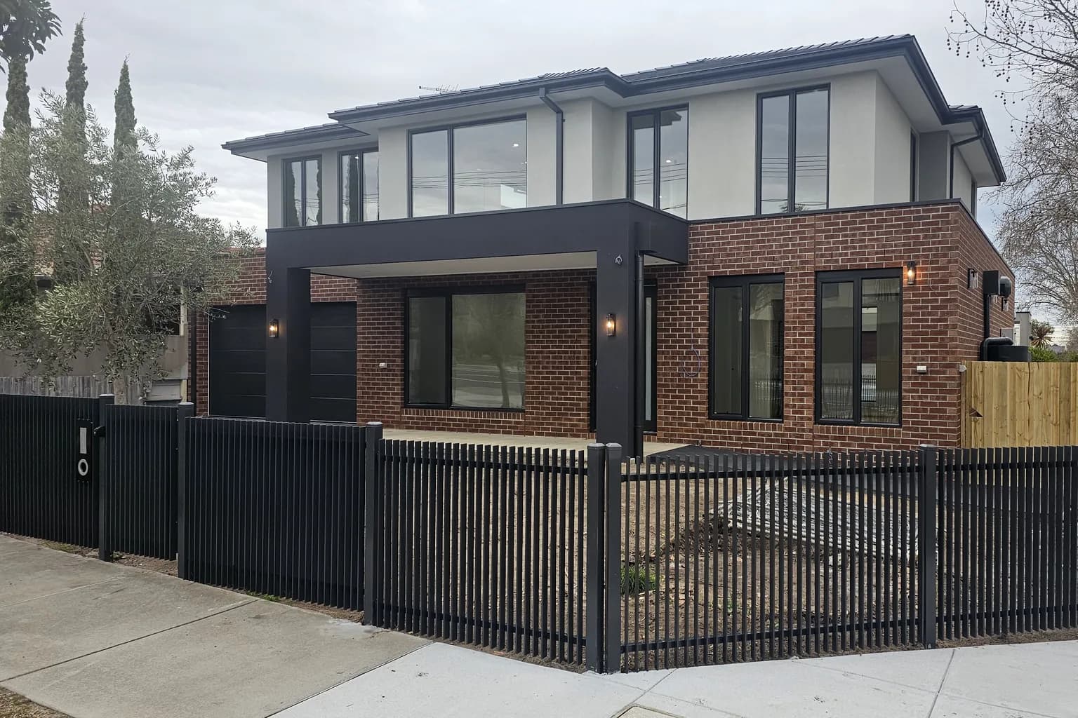 A two storey brick and render townhouse with a charcoal portico and slatted fence, built by NE Homes in Oakleigh