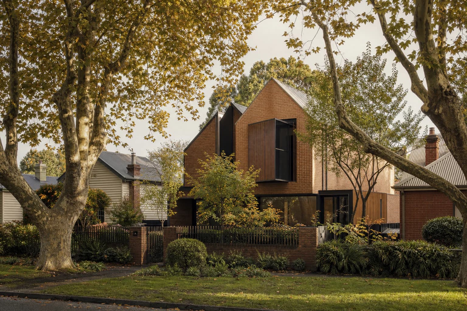 A contemporary gabled brick and timber home standing between older weatherboard and brick houses on a street lined with mature plane trees