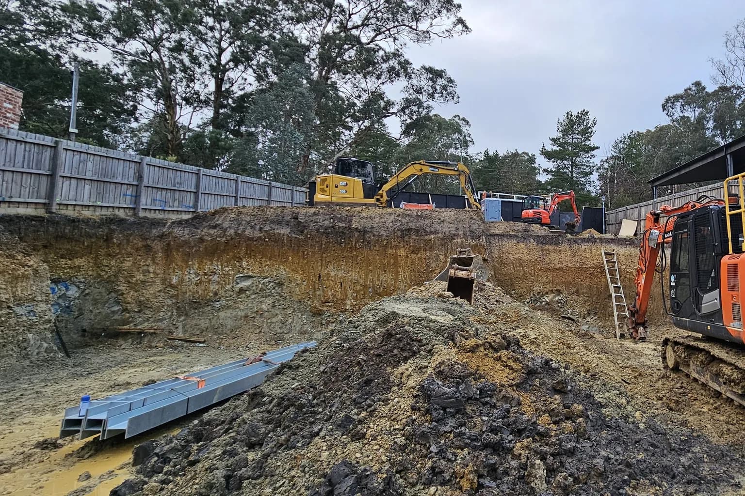 Excavated building platform with a deep cut face and machinery working behind it on a sloping residential site in Warrandyte