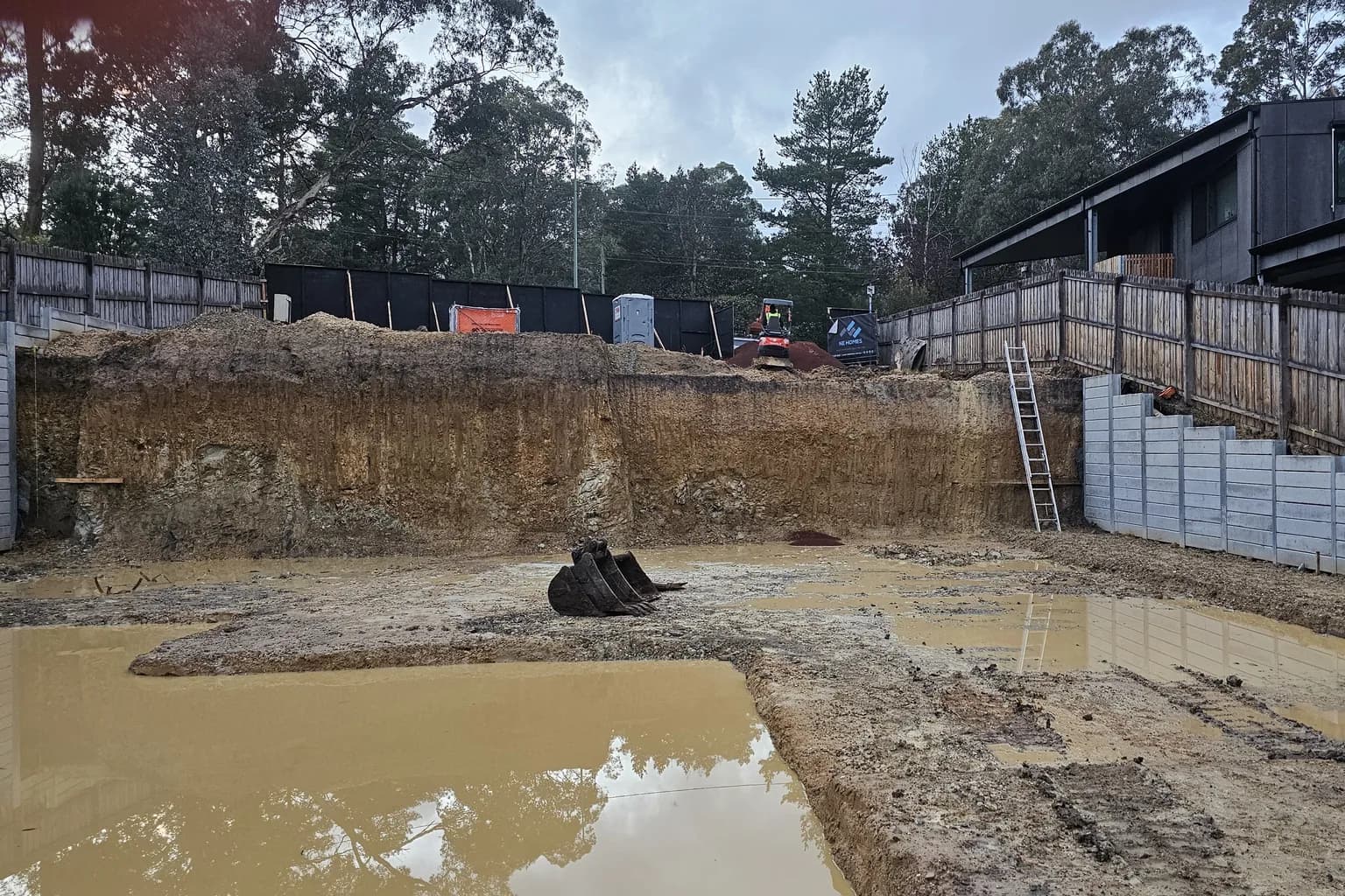 Rainwater lying on an excavated building platform below a cut face and stepped retaining on a sloping site in Warrandyte