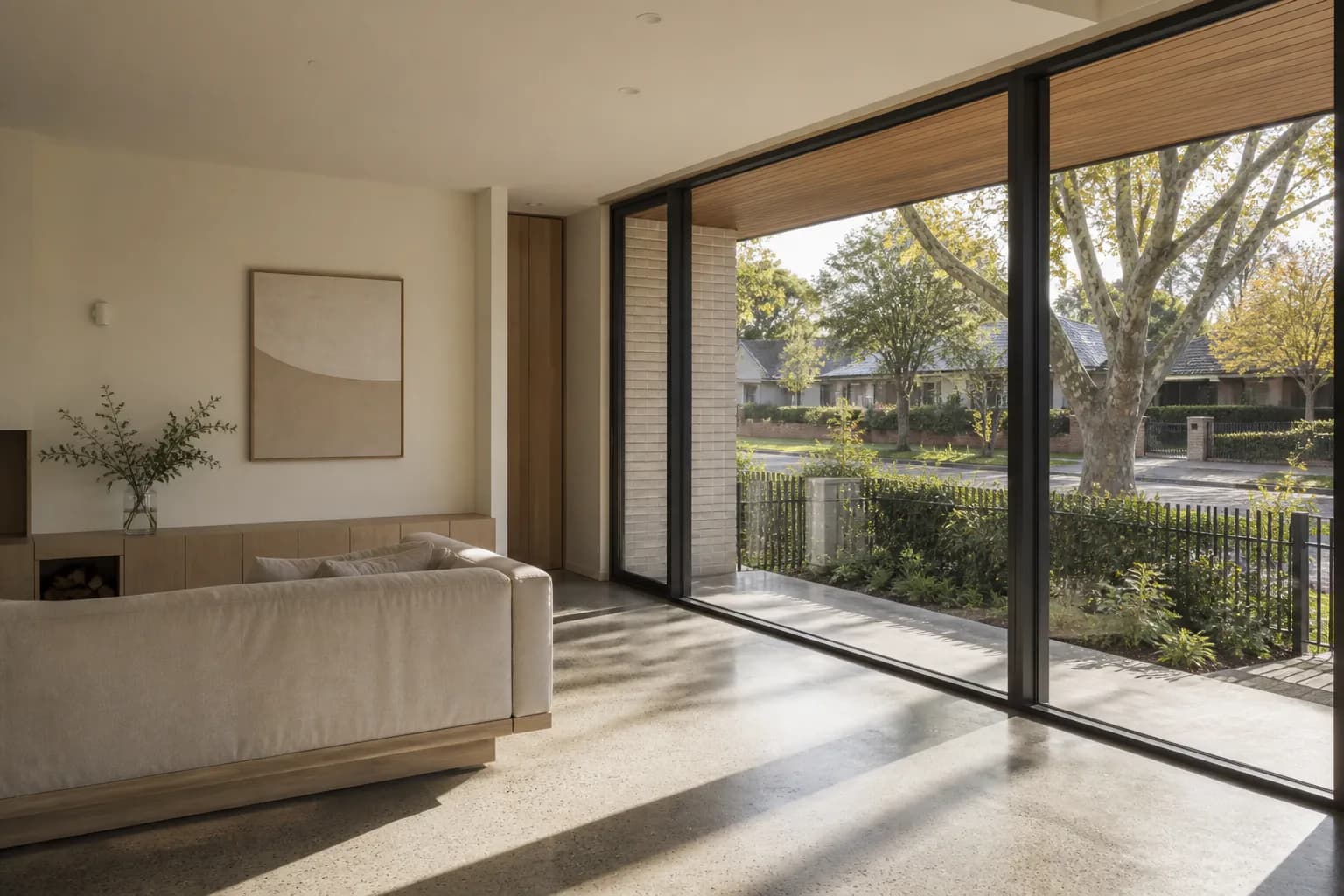 Low winter sun entering a living area through full-height glazing and reaching deep across a polished concrete floor, with a timber-lined eave shading the opening above