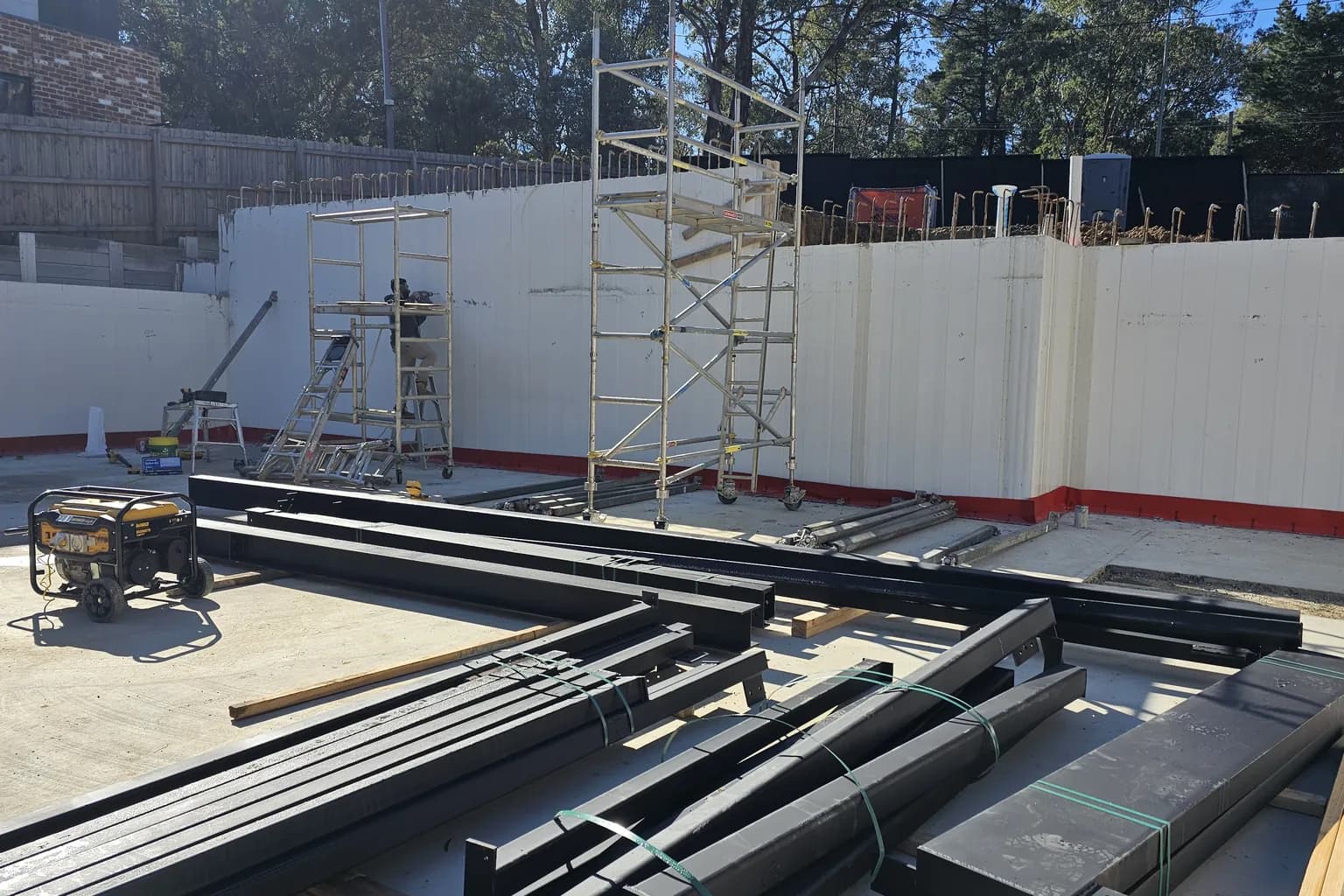 Steel beams laid out on a new concrete slab with scaffold towers against white formwork walls on a house under construction in Warrandyte