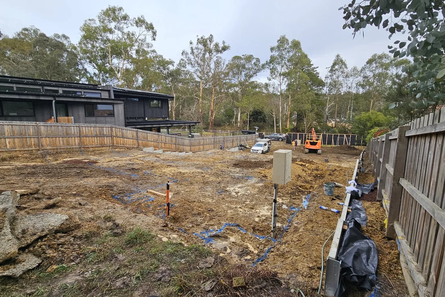 Cleared sloping building site among tall trees with a set-out peg, a service pit and a wrapped drain running along the boundary retaining in Warrandyte