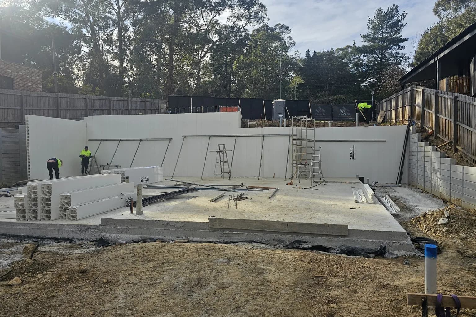 New concrete slab with white formwork walls for the lower level built into the cut of a sloping block beside a stepped boundary retaining wall in Warrandyte
