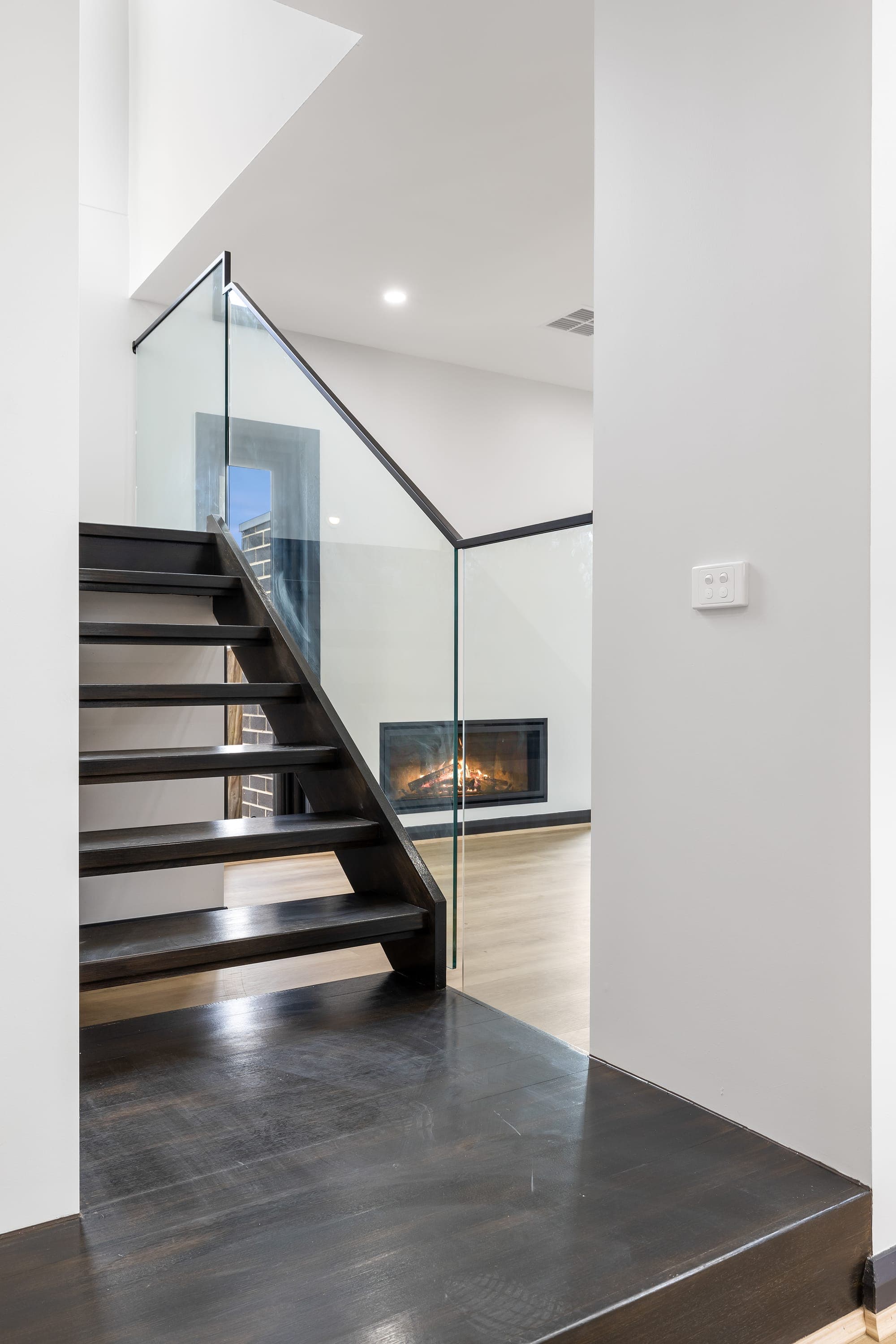 Project Solstice, dark timber staircase with glass balustrade and fireplace