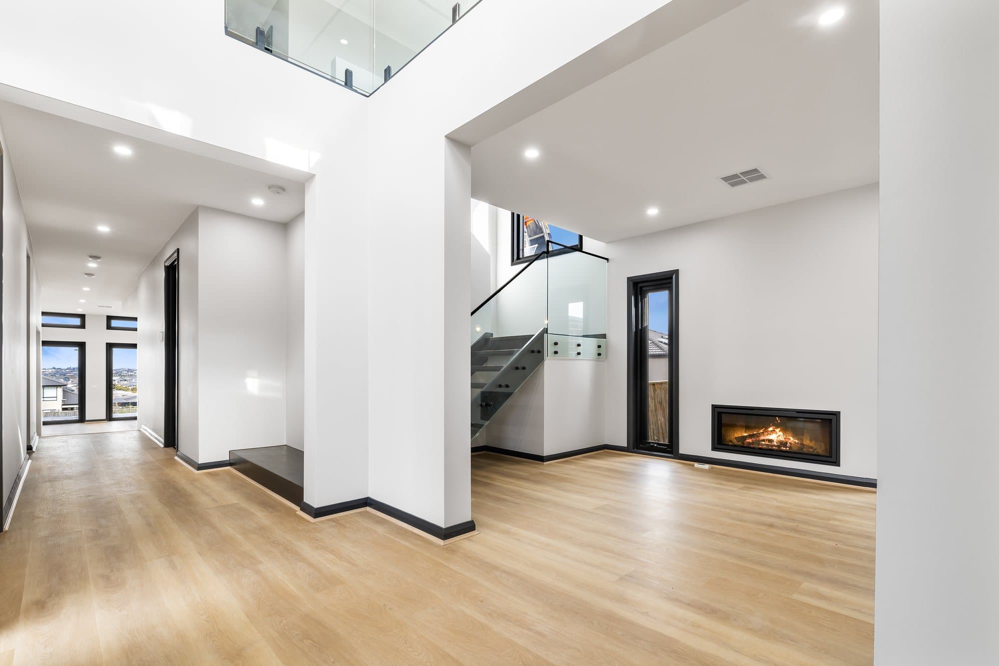 Hallway opening via a short flight of steps to a living room with a gas fireplace, below an open void with a glass balustrade